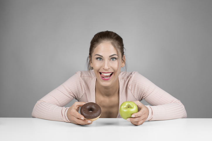 Young Woman Choosing Between Donut And Apple